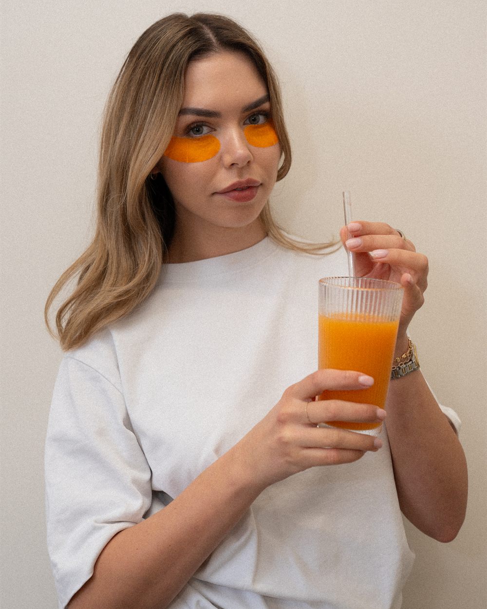 Faye Knox holding a glass of fresh juice, wearing under-eye masks